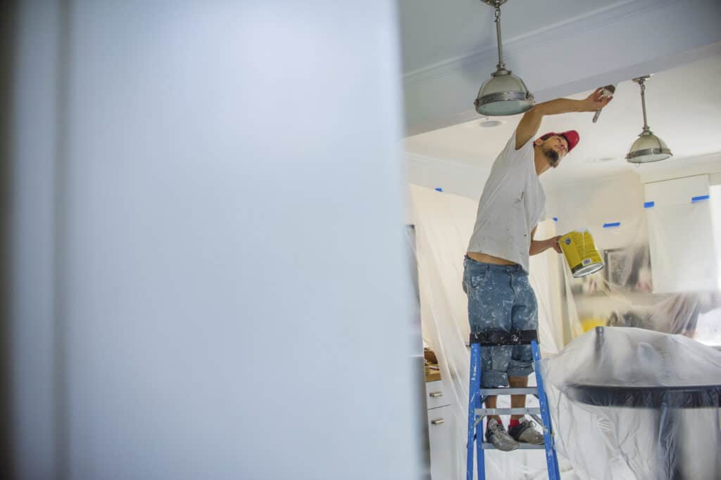 Interior painting with a worker on a ladder applying paint to the ceiling.